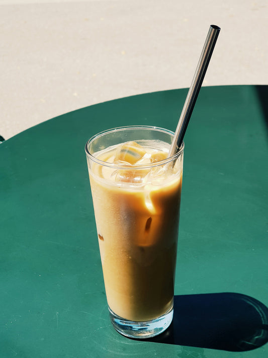 A glass of iced coffee with a swirl of sea-green gel being stirred in, bright modern kitchen counter, natural light.