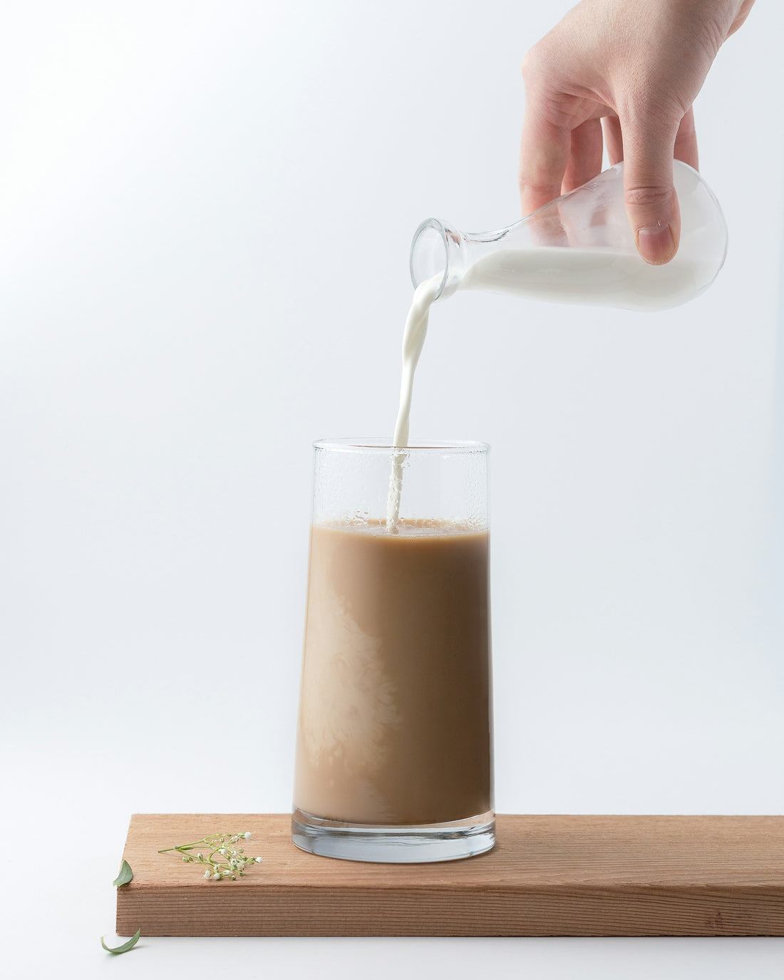 Someone at a kitchen counter pouring steamed milk into a spiced chai latte, warm cozy morning light.