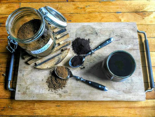 A steaming mug of coffee on a wooden table with a small dish of dark mushroom powder nearby, soft morning light, cozy home kitchen setting.