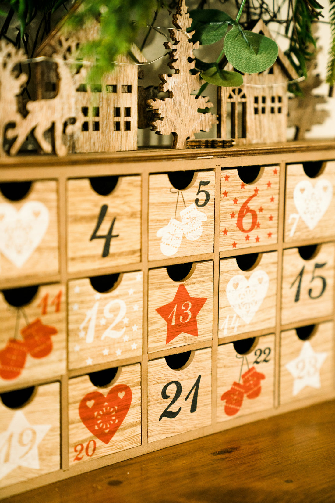 A festive advent calendar with small numbered doors on a table, warm string lights, coffee and tea mugs nearby.