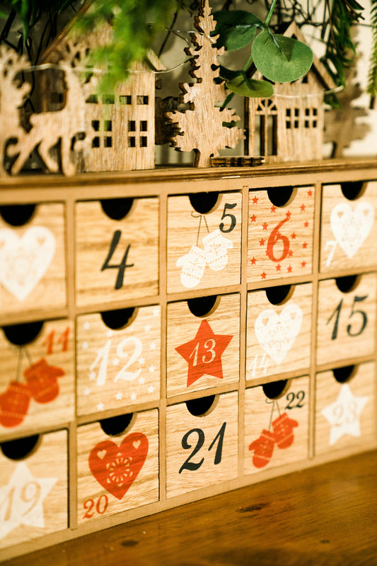 A festive advent calendar with small numbered doors on a table, warm string lights, coffee and tea mugs nearby.