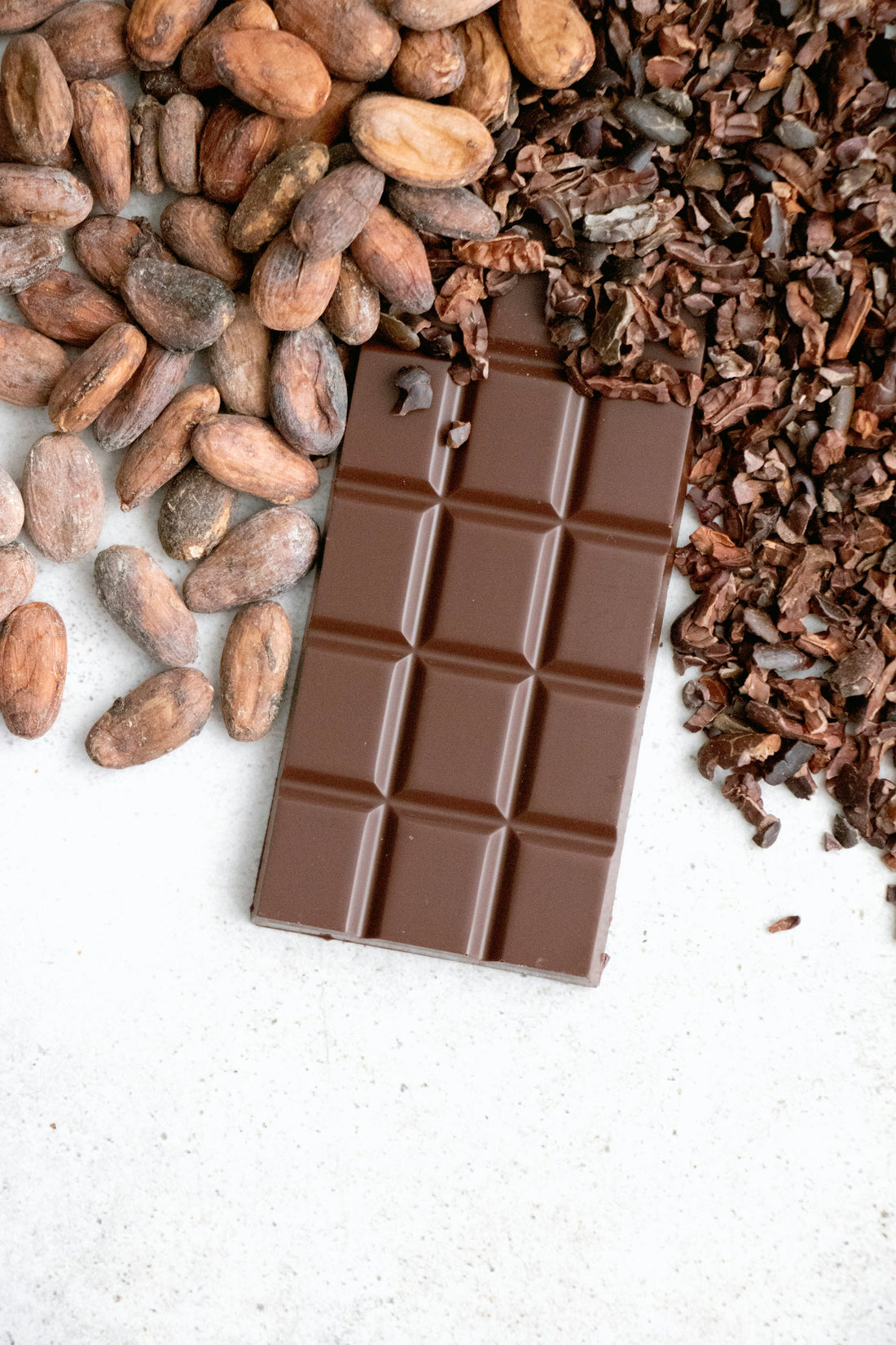 A side-by-side of raw cacao nibs and cocoa powder in small bowls on a wooden table, warm kitchen light.