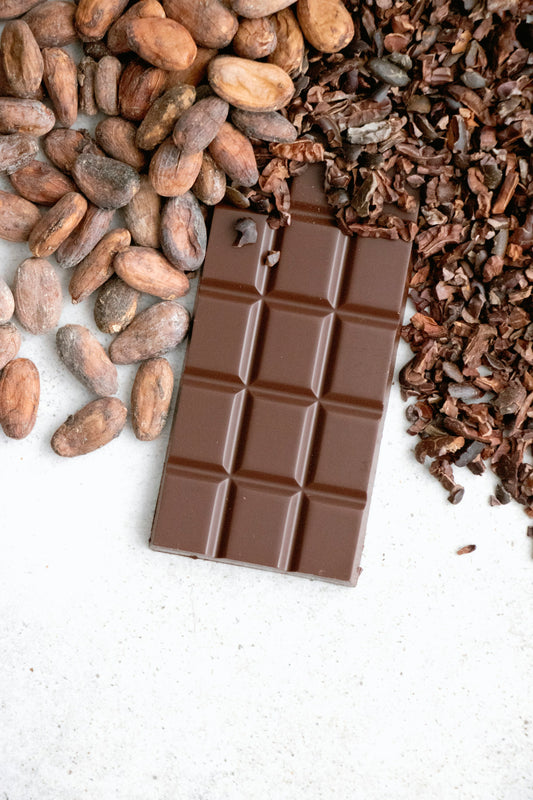A side-by-side of raw cacao nibs and cocoa powder in small bowls on a wooden table, warm kitchen light.