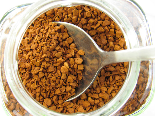 A single mug of coffee next to a small jar of coffee crystals on a travel-friendly counter or camping table.