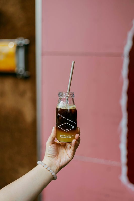 A hand grabbing a bottled iced coffee from a fridge or tote bag, quick grab-and-go morning lifestyle shot.