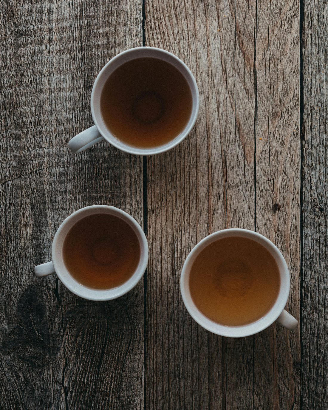 Two ceramic cups side by side, one with vibrant whisked matcha, one with steeped green tea, on a wooden table in natural light.
