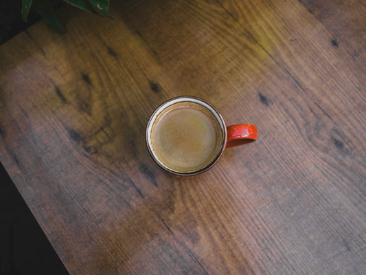 A row of coffee mugs each paired with a different flavor cue, cinnamon sticks and vanilla pods scattered nearby on a wooden table.