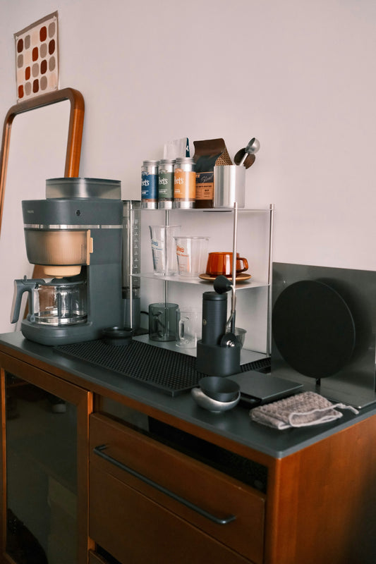 A styled home coffee and tea station on a counter with mugs, syrups, and a carafe, warm hosting atmosphere.