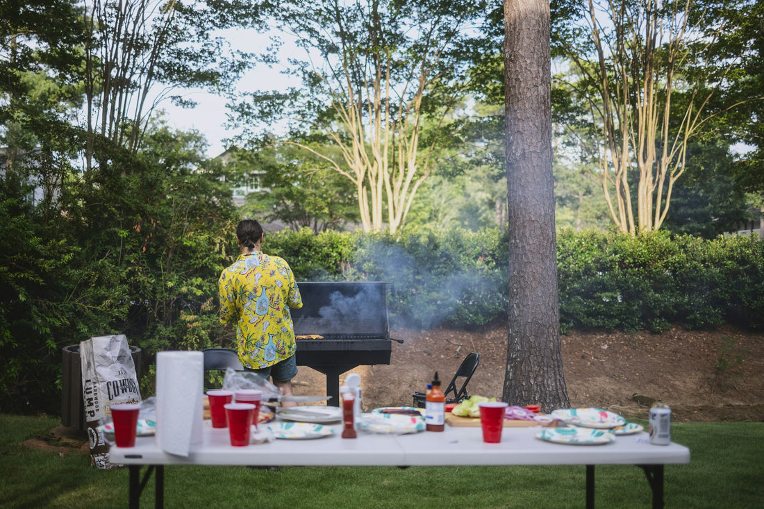 A backyard grill scene with smoke rising, tongs and a rack of ribs, warm late-afternoon cookout light.