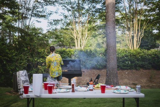 A backyard grill scene with smoke rising, tongs and a rack of ribs, warm late-afternoon cookout light.